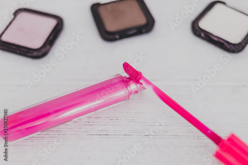 colorful lipglosses surrounded by other make-up products on wooden desk photo