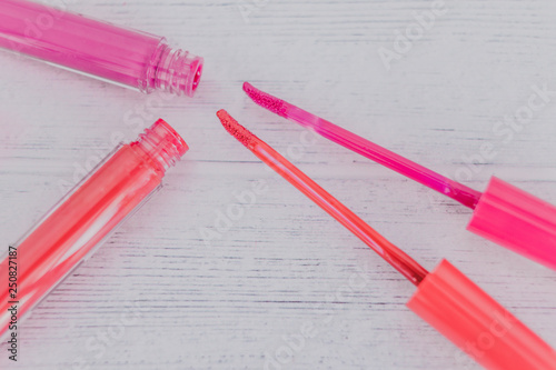 close-up of pink and orange lipglosses or liquid lipsticks on light wooden table photo