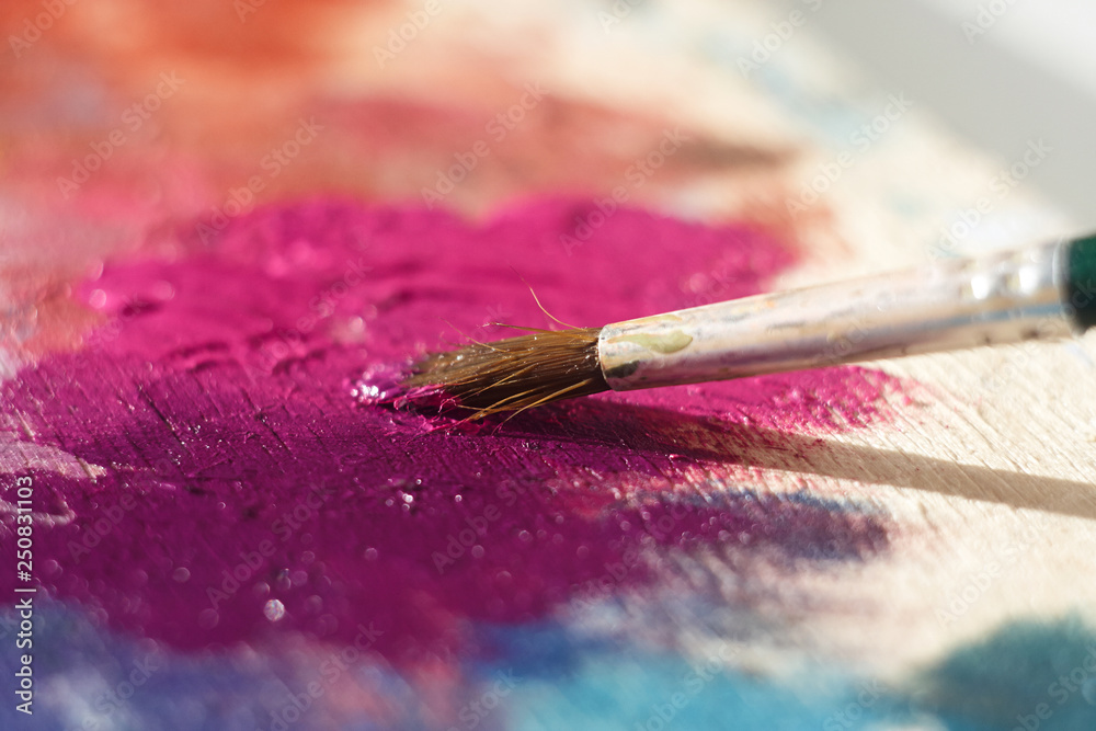 The paint brush mixes pink oil paint on a wooden palette illuminated by the sun The paint brush mixes pink oil paint on a wooden palette illuminated by the sun