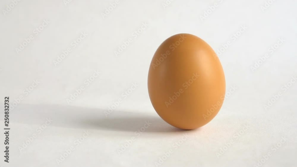 The egg spin by hand slow motion. A brown egg spinning on a white table. Showy easter background. Close up.