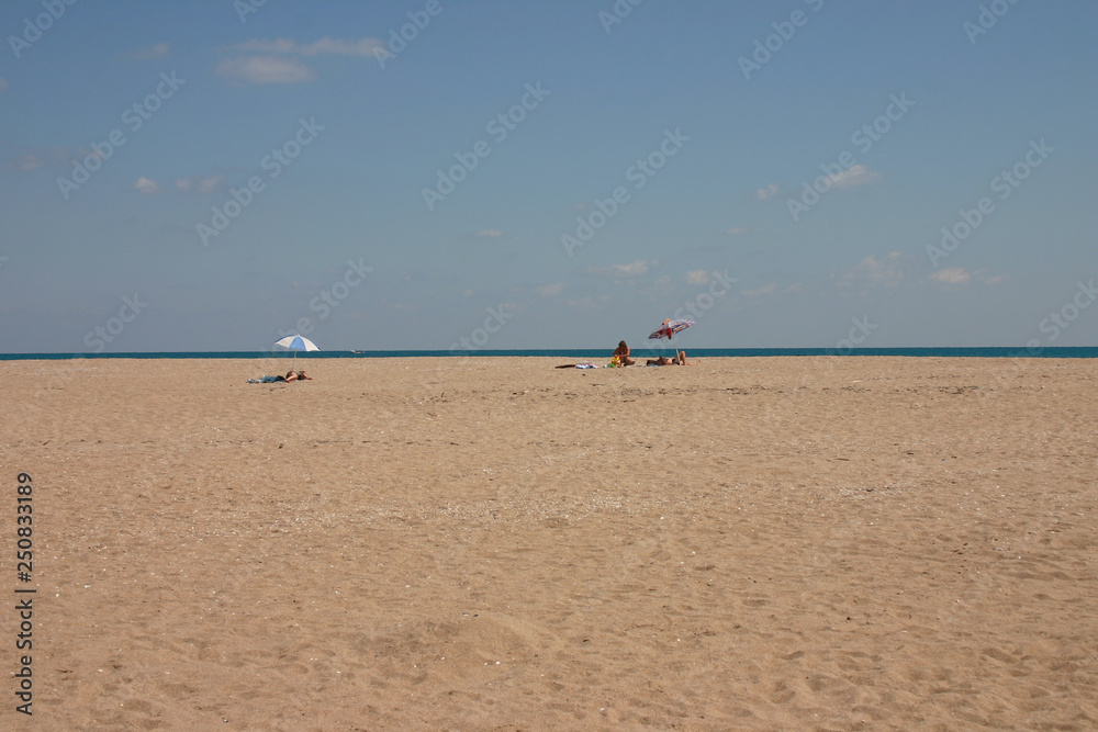 Spacious lonely beach by the sea. Only three tourists rest under their umbrellas in the distance. There is a boat in the sea. Spacious lonely beach by the sea. Only three tourists rest under their umbrellas in the distance. There is a boat in the sea.