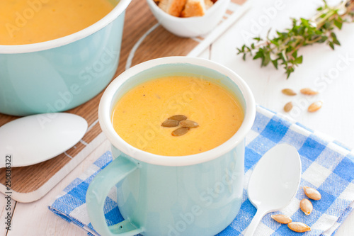 Pumpkin soup in blue enamelled mug with pumpkin seeds, horizontal