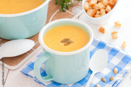 Pumpkin soup in blue enamelled mug with pumpkin seeds, horizontal
