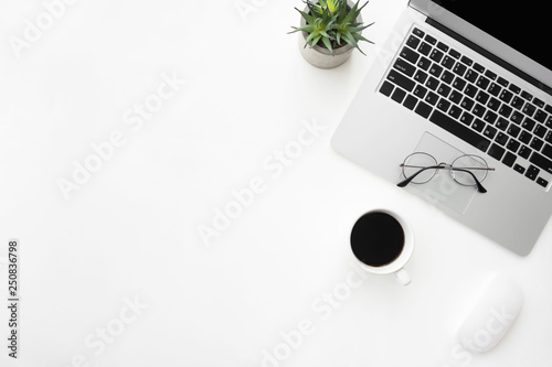 White office desk table with laptop computer, cup of coffee and supplies. Top view with copy space, flat lay.