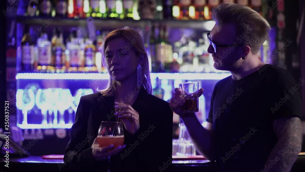 Handsome bearded guy in glasses with an alcoholic cocktail comes up to a girl standing with a cocktail at the bar counter. The man made an indecent proposal to the girl and the girl went away.