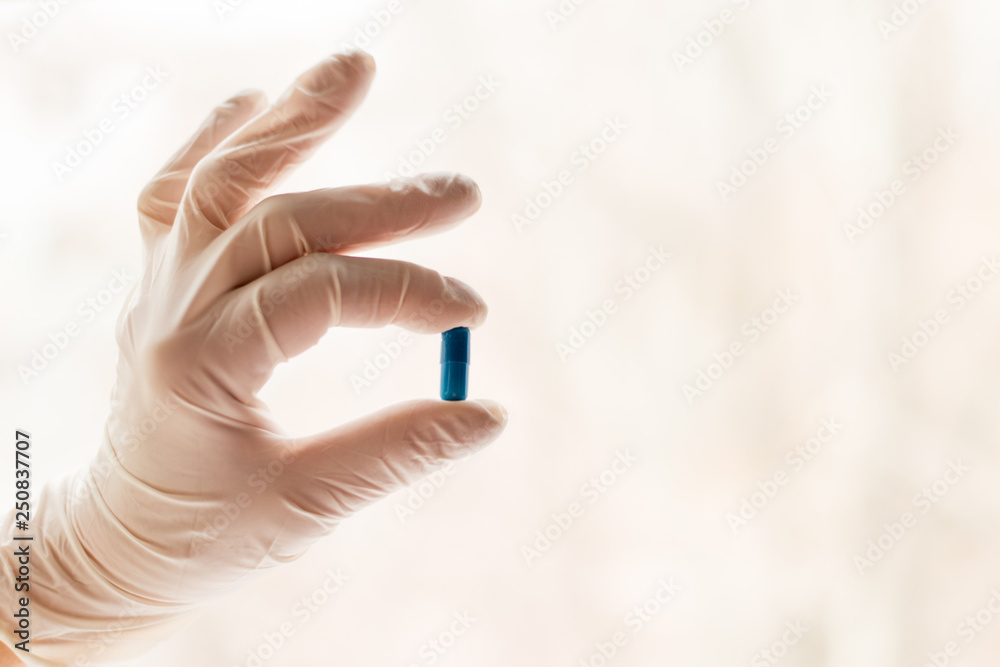 Fototapeta premium Hands in medical gloves holding capsule. medicine background