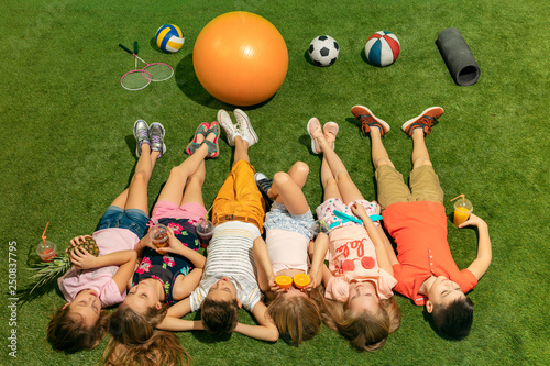 Group of happy children playing outdoors. Kids having fun in spring park. Friends lying on green grass. Top view portrait photo