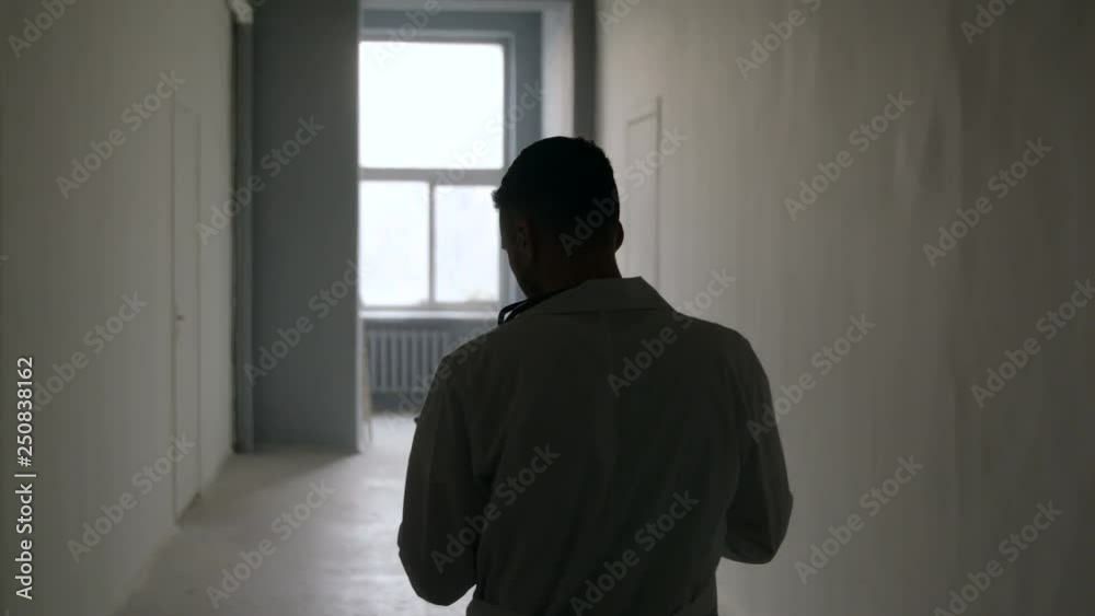 A silhouette of a doctor is walking along a dark hospital A silhouette of a doctor is walking along a dark hospital