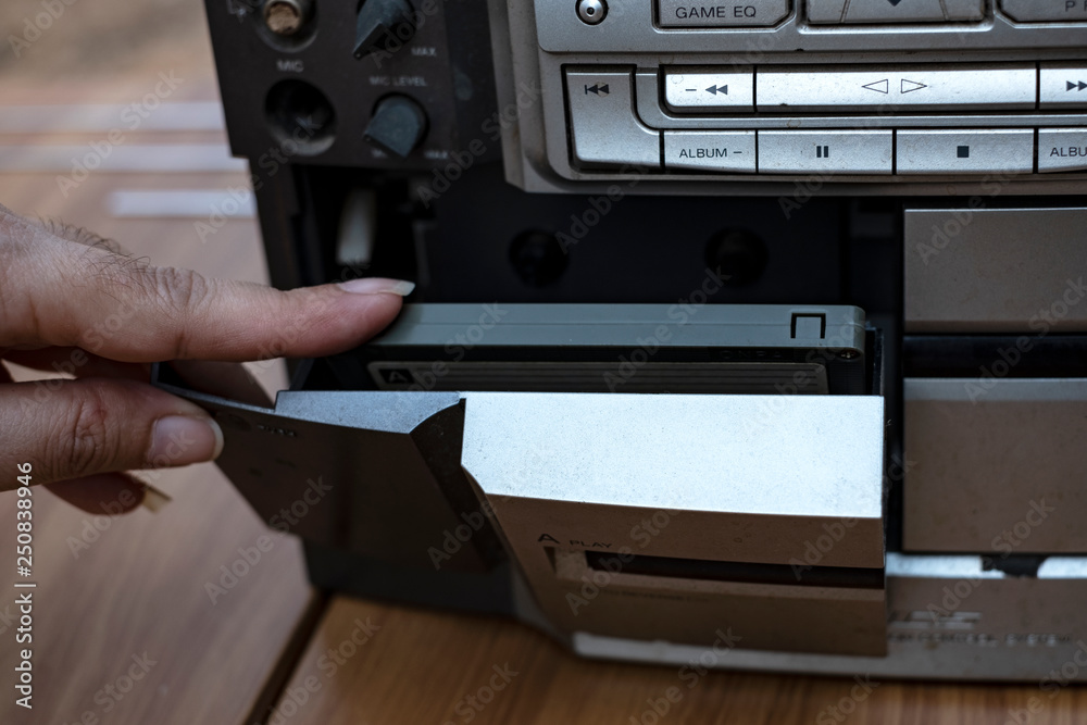 Obraz premium Women hand putting cassette into old fashioned audio tape player on top desk wood background