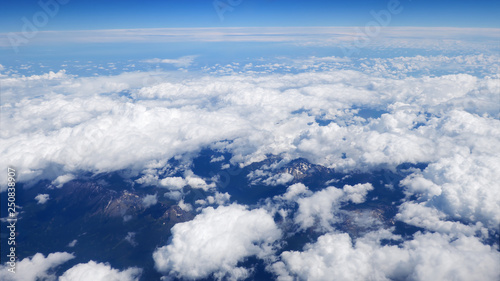 Fototapeta Naklejka Na Ścianę i Meble -  Flying over fluffy white clouds with a partial view of the rural landscape far beneath. Picturesque moving cloudscape view from airplane window.