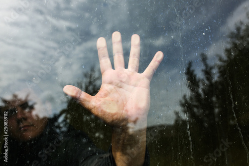 Man is holding hand on the glass window. Reflection of a guy with a nature on background. Lifestyle concept.