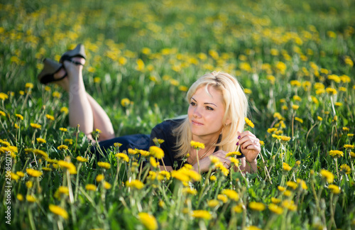 Image of pretty woman lying down on dandelions field, happy cheerful girl resting on dandelions meadow, relaxation outdoor in springtime, vacation 