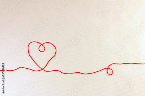 Red thread, heart and tangle on light craft paper background, top view