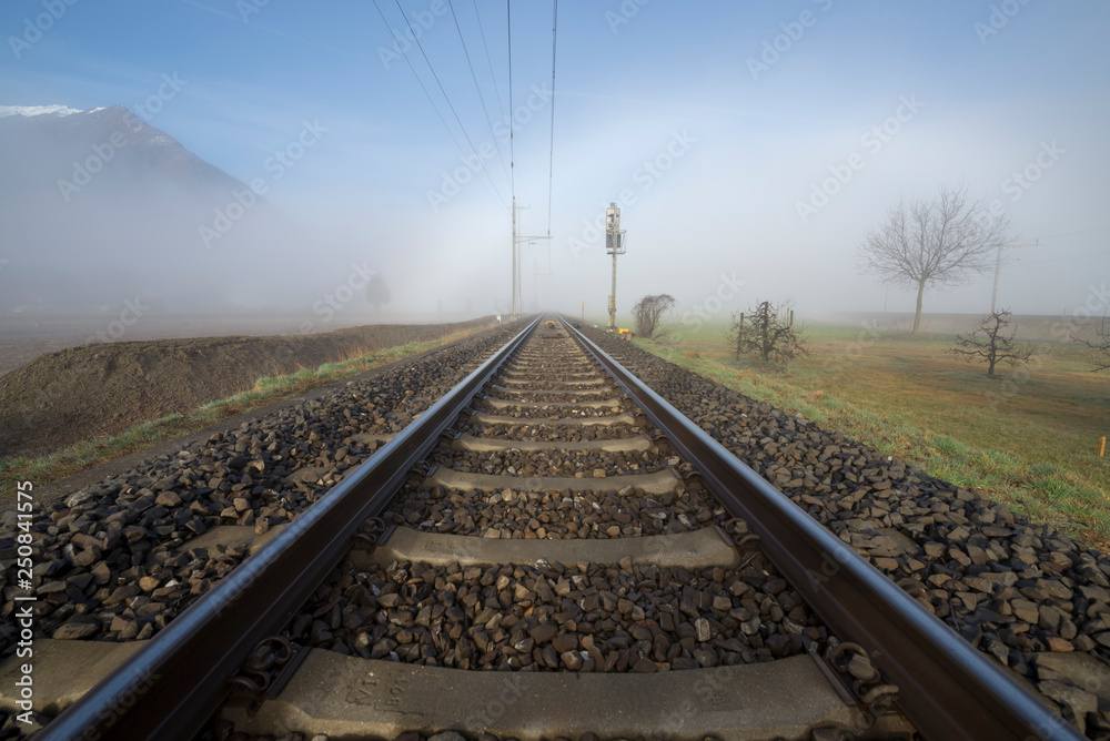 Fototapeta premium Railroad Tracks in the Fog and Mountain in Switzerland.