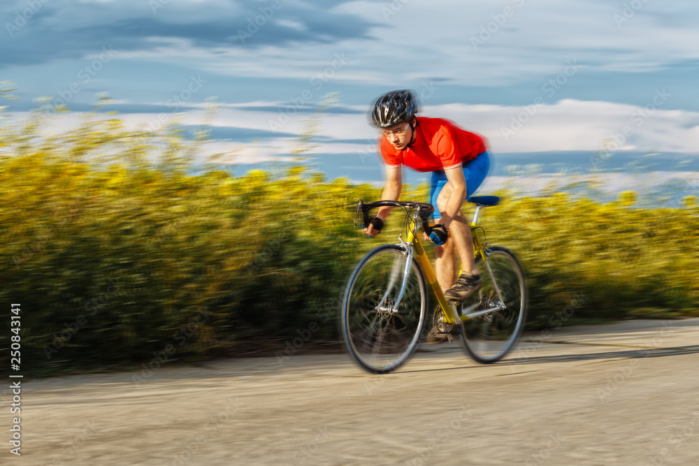 Fototapeta premium A cyclist rides on a road bike quickly along fields of sunflowers.