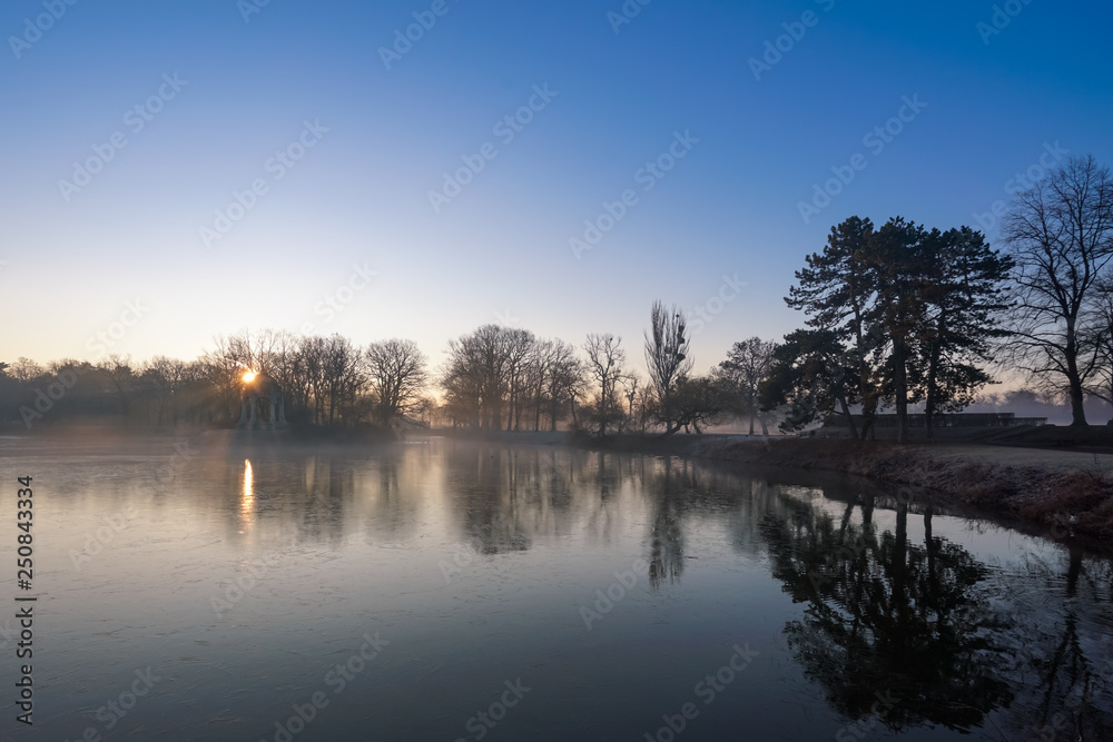 Tiefstehende Sonne und Nebel im winterlichen Stadtpark von Magdeburg am Adolf Mittag See