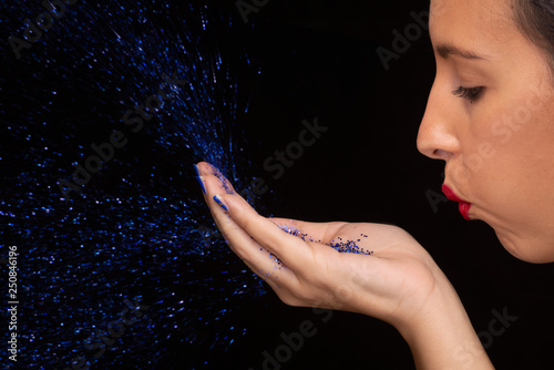 ragazza soffia brillantini azzurri su fondo nero photo