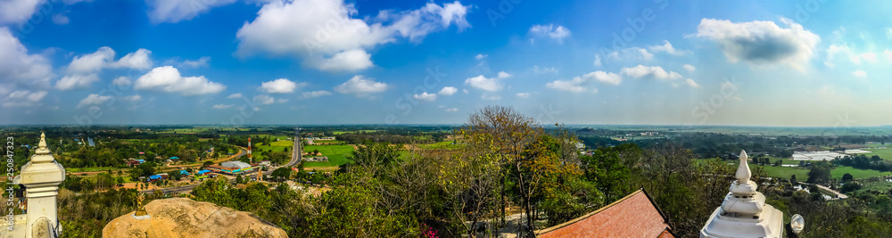Panorama view over highway from hilltop around with countryside green rice fields and blue sky background. The provincial highway with cars and trucks crossing the hills at Phichit province, Thailand.
