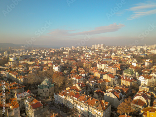 View from the height of the old town with low houses with tiled roofs and bare trees against the blue sky and gray clouds on the horizon © Kseniya