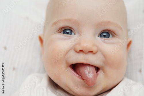 Cute five-month baby with blue eyes lies and smiles  shows tongue. Maternal care. Childcare. Close.