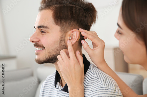 Woman putting hearing aid in man's ear indoors