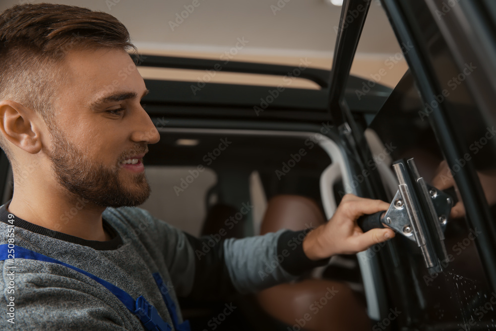 Skilled worker washing car window before tinting in shop Skilled worker washing car window before tinting in shop