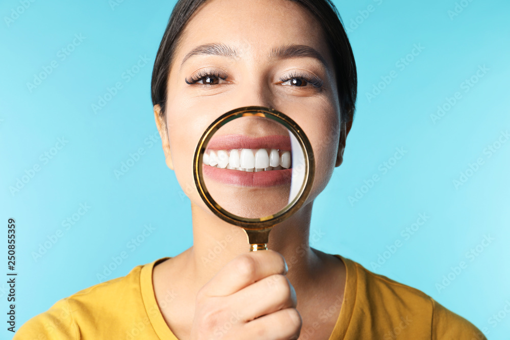 Young woman with healthy teeth and magnifier on color background, closeup Young woman with healthy teeth and magnifier on color background, closeup