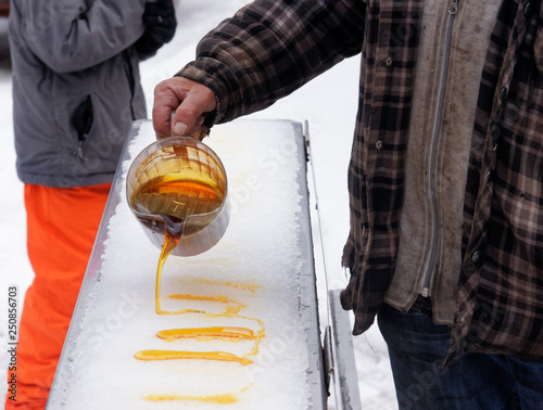 A man pouring hot liquid maple syrup onto ice, where it cools to form maple taffy