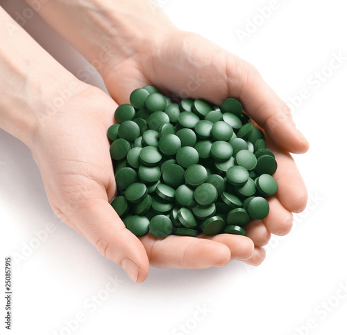 Woman holding heap of green spirulina pills on white background, top view
