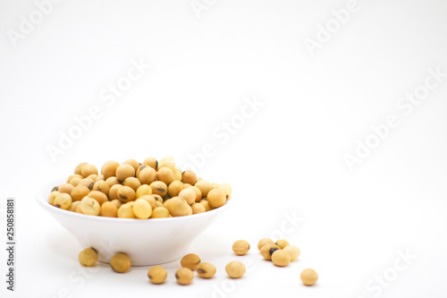 Soy seeds in white bowl and some drop out on white background