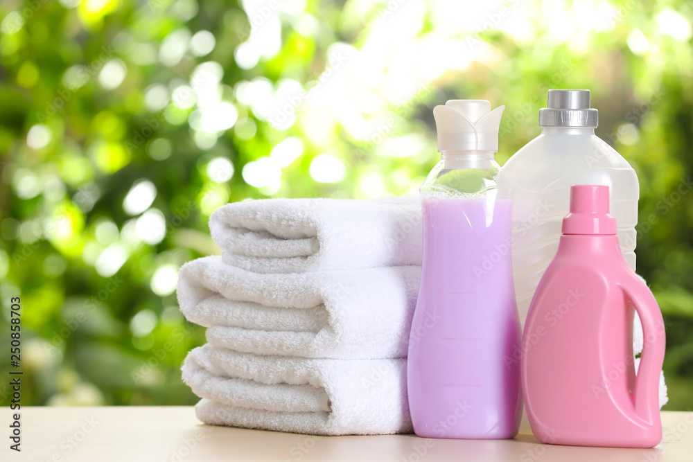 Soft bath towels and laundry detergents on table against blurred background Soft bath towels and laundry detergents on table against blurred background