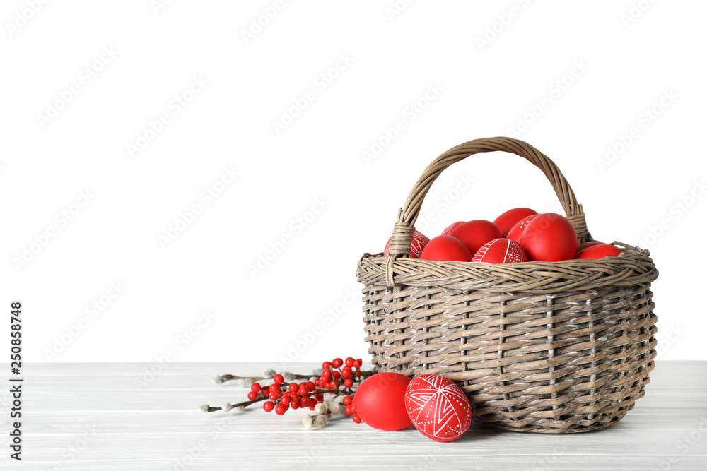 Wicker basket with painted red Easter eggs on table against white background, space for text Wicker basket with painted red Easter eggs on table against white background, space for text