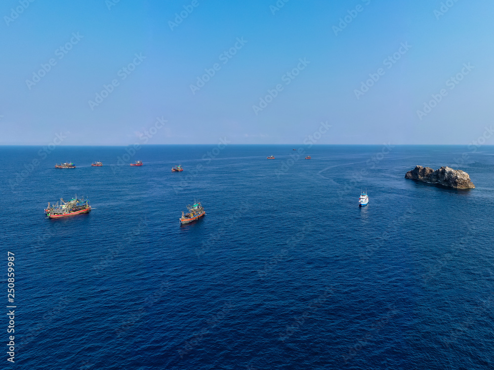 Aerial drone view of a fleet of large fishing trawlers surrounding a single SCUBA diving boat at the Black Rock dive site in the Mergui Archipelago, Myanmar