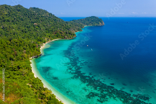 Aerial drone view of a beautiful tropical island surrounded by coral reefs and covered with lush, green jungle (Kyun Phi Lar, Myanmar)