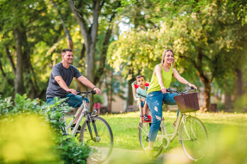 Happy family. Smiling father and mother with kid on bicycles having fun in park..