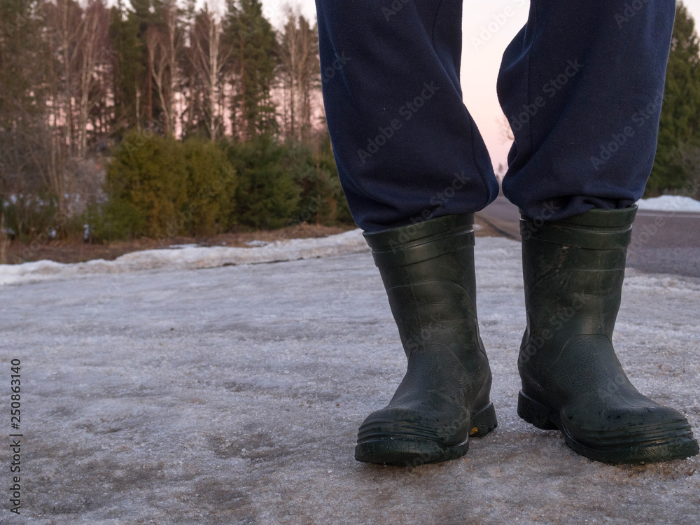 Rubber boots for work use. A construction worker on grey asphalt, cold outside