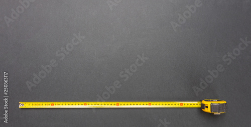 Yellow measure tape isolated on black color background, top view, copy space