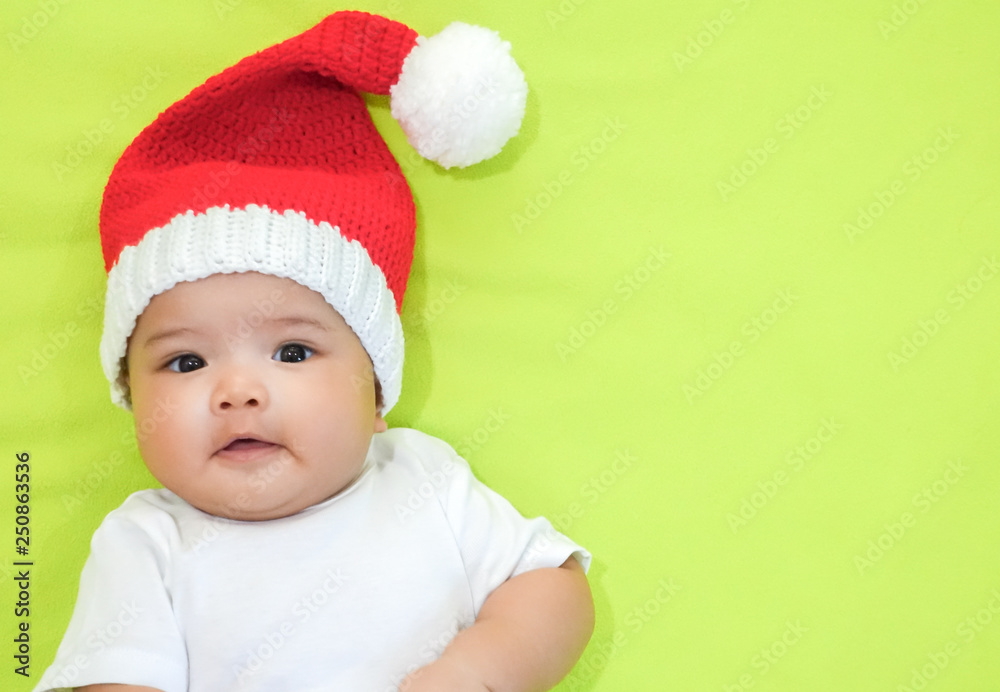 Newborn Asian baby is wearing red Christmas knitting hat and white dress on light green background Newborn Asian baby is wearing red Christmas knitting hat and white dress on light green background
