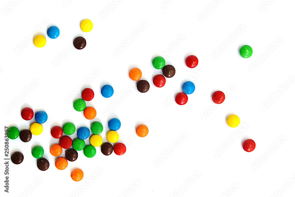 A scattering of colored small chocolates on a white background.Small colored candies