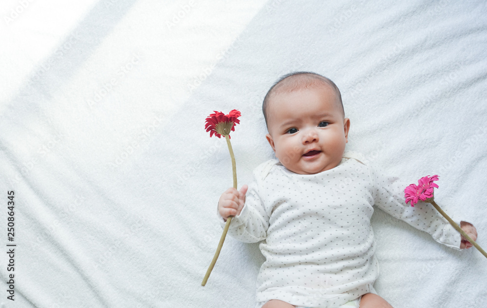 Asian baby girl is holding red and pink flowers on white towel background  with sun light