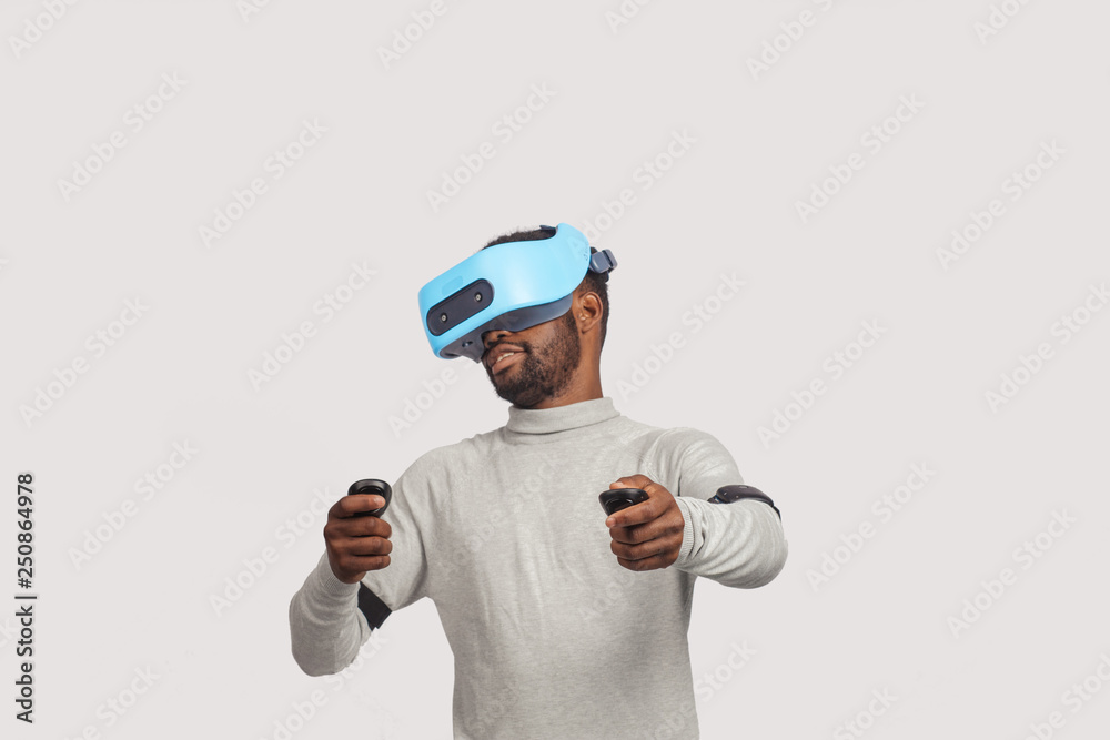 Fototapeta premium Stylishly dressed african guy using new VR technology headset, learning material and getting knowledge and practice through 3D video glasses. Virtual education concept