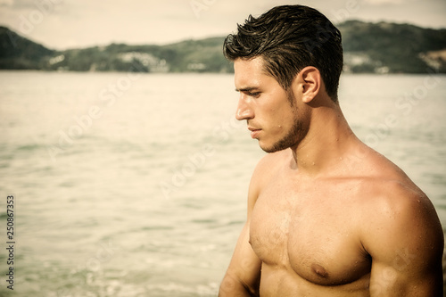 Attractive young man in the sea getting out of water with wet hair, looking away to a side