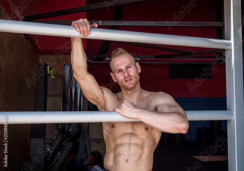 Handsome muscular young man standing against horizontal bars, looking at camera