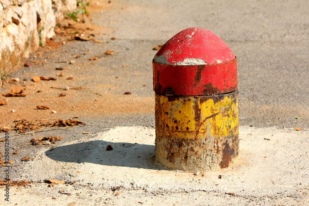 Colorful old dilapidated partially rusted concrete and metal parking security barrier or bollard mounted on asphalt to prevent parking and car entrance on warm sunny day