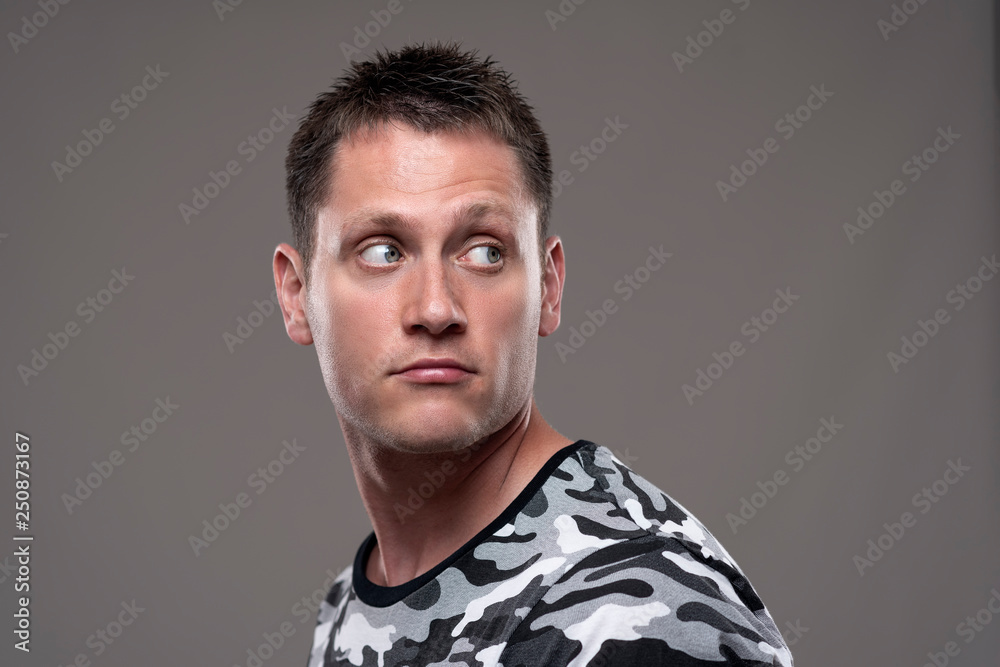 Obraz premium Handsome young adult man in army shirt looking back over the shoulder at copy space on gray background. 