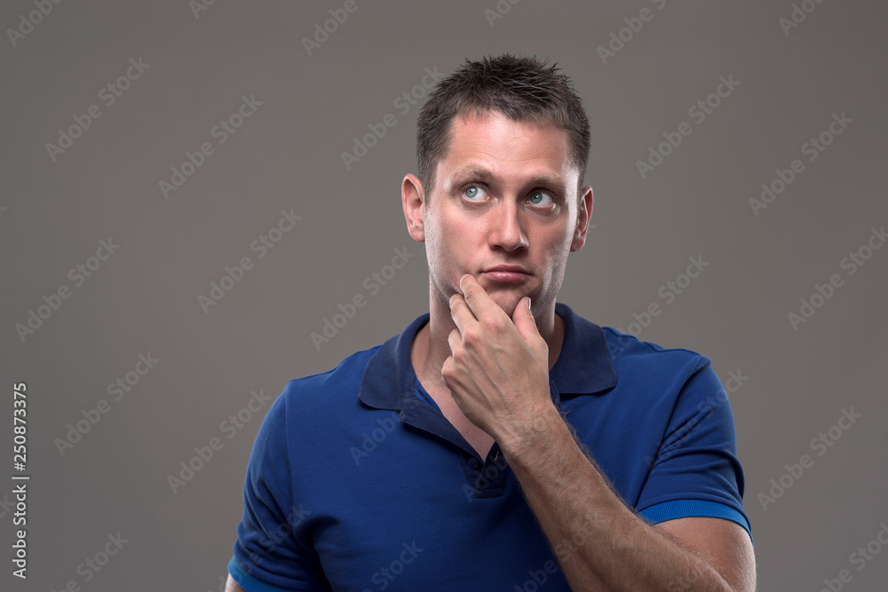 Portrait of thoughtful serious uncertain young adult man looking up thinking with hand on chin on gray background. Portrait of thoughtful serious uncertain young adult man looking up thinking with hand on chin on gray background.