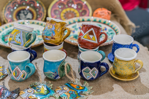 Variety of Colorfully Painted Ceramic Pots in an Outdoor Shopping Market. pottery in the shop window. Clay cups and plates © jollier_