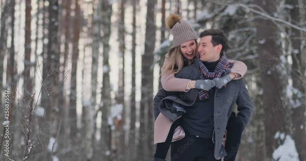 Happy Couple is Playing Winter Game Outside Enjoying Sunlight and Warm Winter Weather in the Mountains. Strong Boy is Carrying Girlfriend on His Shoulders and Whirls Her Happy Couple is Playing Winter Game Outside Enjoying Sunlight and Warm Winter Weather in the Mountains. Strong Boy is Carrying Girlfriend on His Shoulders and Whirls Her