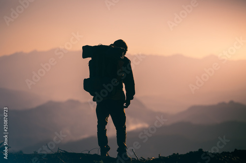 the accomplishment of tourist with backpack standing on the mountain at sunset background. travel silhouette concept.