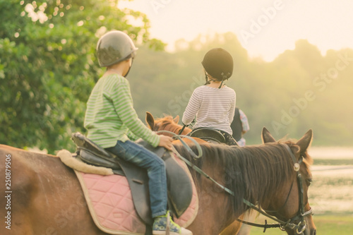 Kids learn to ride a horse near the river before sunset.
